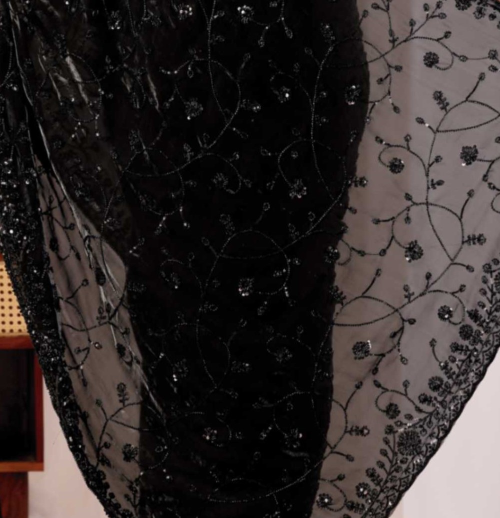 The Black Onyx Sequin Heritage Saree The Black Onyx Sequin Heritage Saree + Embrace the allure of the night with this stunning midnight onyx saree from Kesari Culture. This piece is a masterclass in monochrome elegance, featuring a luxurious black base completely transformed by shimmering tonal sequins. The intricate embroidery creates a subtle yet captivating texture that dances with the light, making it a sophisticated choice for cocktail parties, evening receptions, and high-glamour events. Paired with a sleek, sleeveless V-neck blouse, this ensemble offers a contemporary silhouette while maintaining the timeless grace of traditional attire.